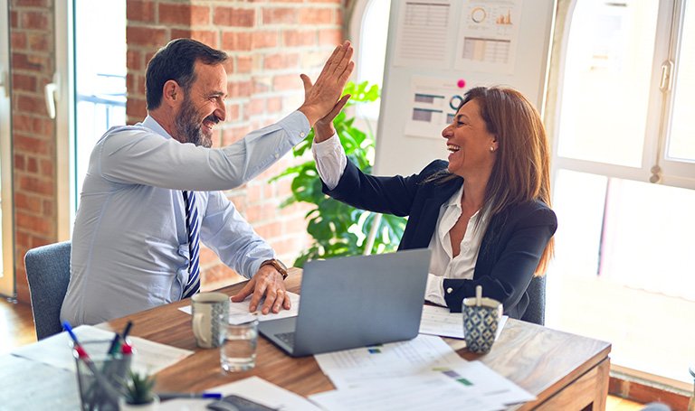 Smiling businessman and businesswoman high five at desk