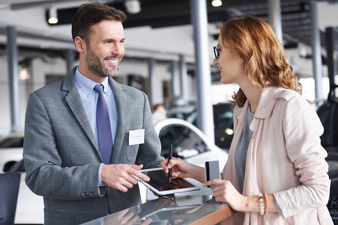 Car salesman in grey suit having a discussion with female customer in light pink top