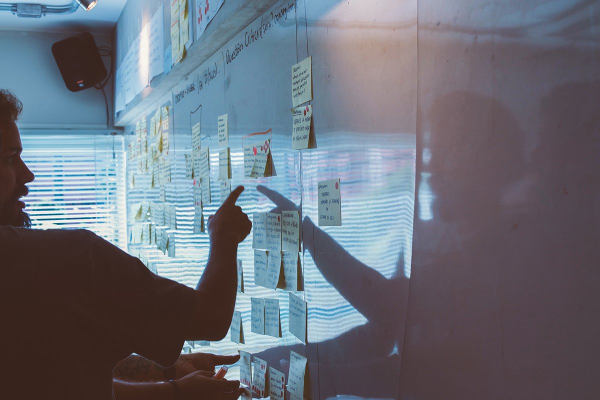 people pointing at a whiteboard with post stick notes on it