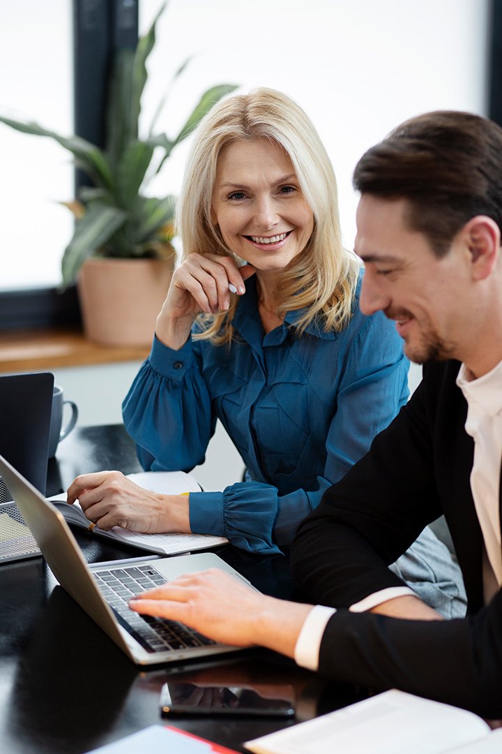 Closeup of business woman with blonde hair wearing a blue shirt having meeting with business man with dark hair wearing a black jacket and white shirt