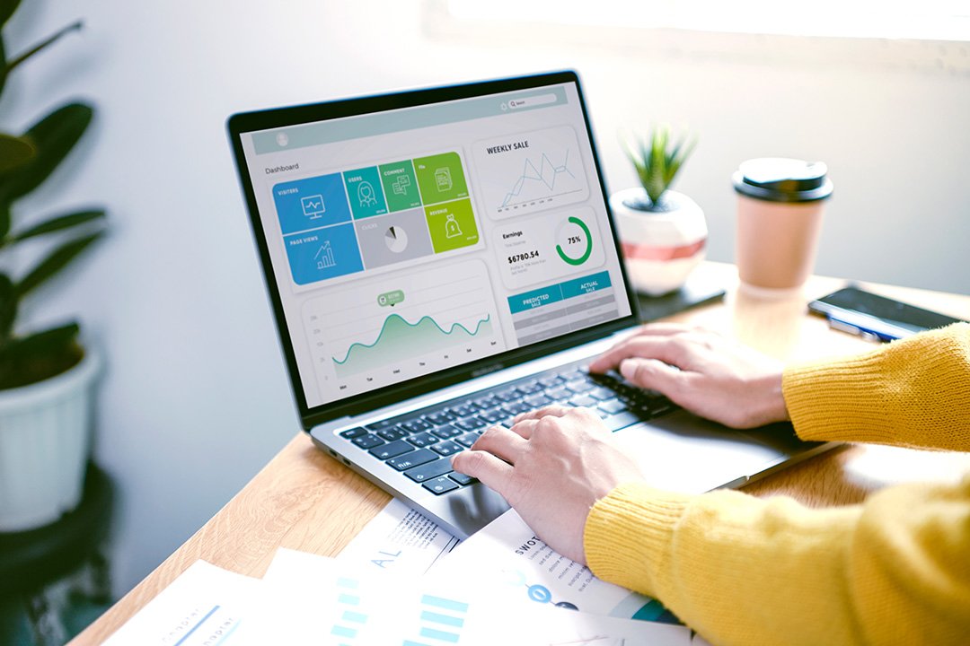 Closeup of woman's hands using laptop with CRM system on screen at a desk in bright office setting