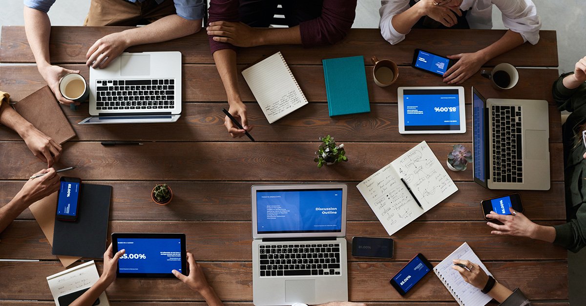 Sales team sat at meeting table with laptops planning business