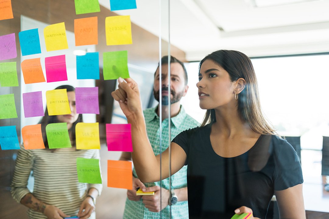 Business meeting with woman pointing to and explaining sticky notes on glass to colleagues