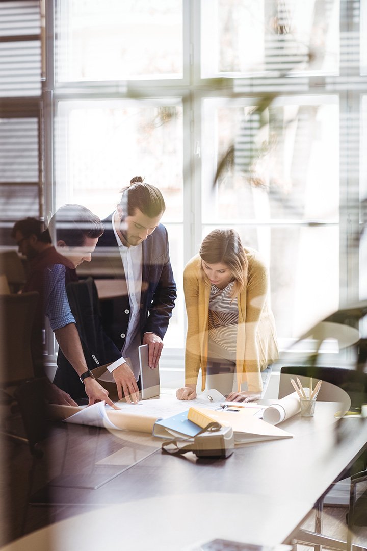 Two men and one woman standing around office table planning something on paper